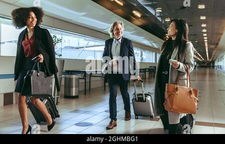 Petit groupe de gens d'affaires qui marchent ensemble dans le terminal de l'aéroport. Les voyageurs d'affaires qui ont des bagages à bord de leur vol. Banque D'Images