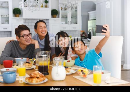 Parents asiatiques souriants avec leur fils et leur fille assis à la table du petit déjeuner prenant le selfie Banque D'Images