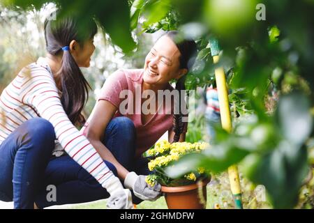 Bonne mère asiatique et fille souriant, portant des gants et travaillant dans le jardin Banque D'Images