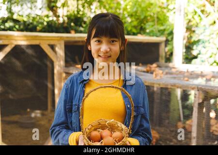 Portrait d'une fille asiatique souriant et tenant le panier, recueillant les œufs de la maison de poule dans le jardin Banque D'Images