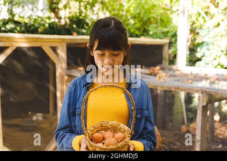 Fille asiatique souriant et tenant le panier, la collecte des oeufs de la maison de poule dans le jardin Banque D'Images