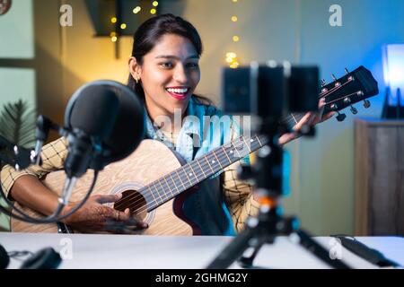 jeune fille influenceur jouant de la guitare pendant le podcast ou la diffusion vidéo en direct pour le public à partir de téléphone mobile à la maison - concept d'art, de passe-temps et de vidéo Banque D'Images