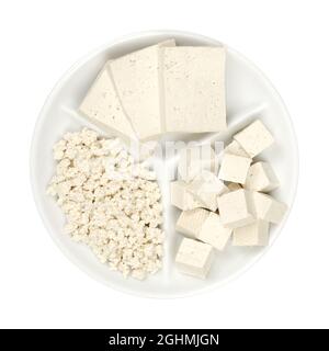 Tofu blanc transformé, sur un petit plateau de service blanc. Trois tranches, cubes et tofu émietté. Caillé de soja à base de lait de soja coagulé. Banque D'Images