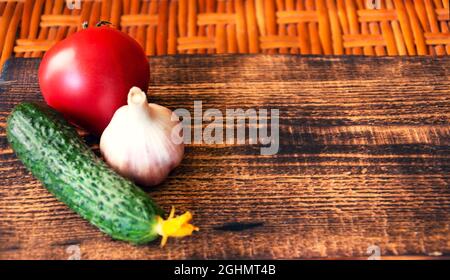 Le concombre vert, la tomate rouge et l'ail reposent sur une planche à découper en bois sur le fond d'une table en bois. Espace libre. Photo de haute qualité Banque D'Images