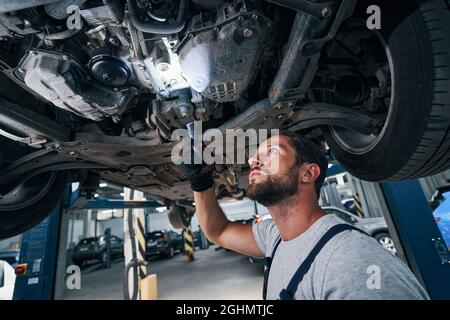 Homme avec lampe de poche sous l'automobile étudiant son dessous Banque D'Images