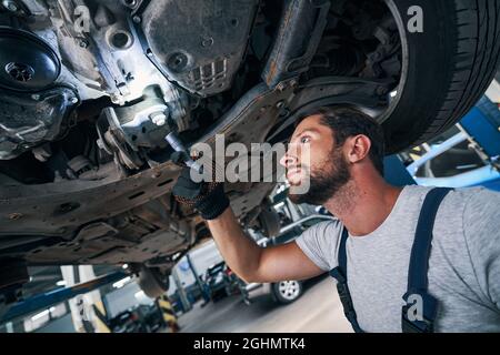 Un réparateur automobile examine le dessous de la voiture à l'aide d'une lampe de poche Banque D'Images