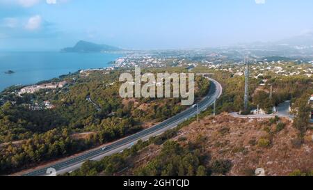 Photo aérienne de la côte des collines et des montagnes d'Altea sur la Costa Blanca d'Espagne. Rue avec arbres des deux côtés peut être vu. Ciel bleu clair en arrière-plan. Horizon de la ville. Banque D'Images