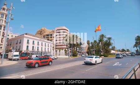 Benidorm, Espagne 18.08.2021 - voitures fonctionnant sur une route à deux voies en Espagne pendant la journée ensoleillée. Bureaux sur le côté. Rue avec palmiers. Drapeau balançant dans le vent. Ciel bleu clair. Banque D'Images