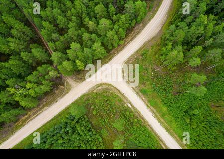 Vue aérienne plein cadre depuis un drone de pays idyllique qui croise des routes en croisement menant à travers des forêts galantes de pins et de bouleaux dans des couleurs vert foncé par temps pluvieux nuageux Banque D'Images