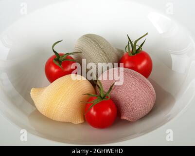 Trois grandes pâtes crues en forme de coquille avec trois tomates fraîches sur une assiette blanche. Banque D'Images