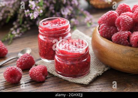 Deux petits pots de confiture de framboises, un bol en bois de framboises rouges fraîches sur une table de cuisine. Banque D'Images