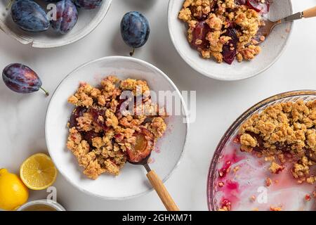 Petit déjeuner savoureux. Tarte aux prunes aux fruits dans des assiettes avec des cuillères et une tasse de thé avec du citron sur une table en marbre blanc. Vue de dessus Banque D'Images