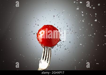 cerise de tomate sur une fourchette dans des éclaboussures d'eau. Arrière-plan noir et blanc Banque D'Images