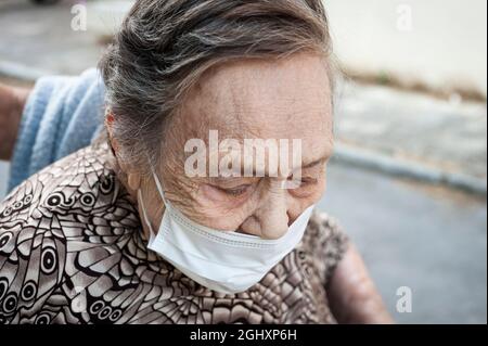 gros plan d'une octogénaire marchant dans un fauteuil roulant avec un aspect crevé, portant un masque de protection Banque D'Images