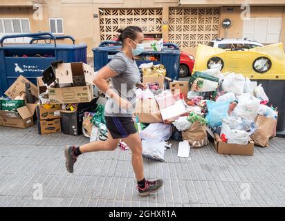 Jogging féminin passant devant des poubelles entassées à côté de conteneurs de recyclage communautaires complets dans la rue en Espagne Banque D'Images