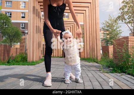 bébé fille avec maman marchant dans la cour de la ville, l'enfant apprend à marcher Banque D'Images