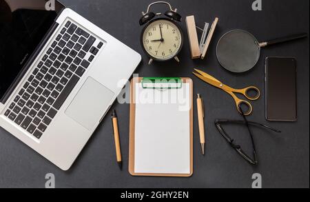 Plan de travail. Presse-papiers vierge, ordinateur portable, téléphone portable et papeterie sur bureau couleur noire, vue du dessus, espace de copie Banque D'Images