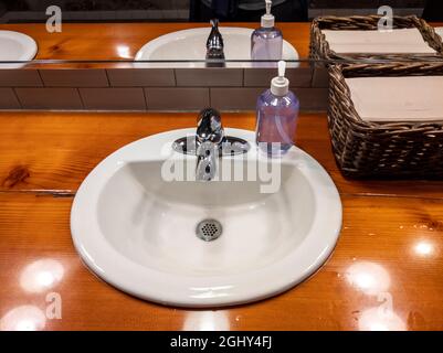 Vue en angle sur un lavabo blanc sur un comptoir en bois à l'intérieur d'une salle de bains de restaurant Banque D'Images