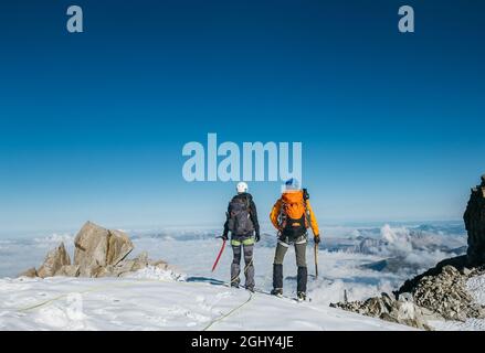 Couple cordage d'équipe connecté avec harnais d'escalade vêtements d'alpinisme habillés avec sacs à dos et haches de glace en profitant de la vue sur le Mont blanc (Mont Banque D'Images