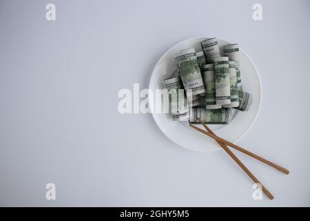 Dollars dans une plaque avec des baguettes de bois sur un fond blanc. Banque D'Images