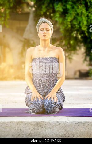 belle fille s'agenouillant avec les yeux fermés pratiquant la méditation à l'extérieur Banque D'Images
