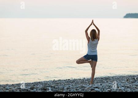 Une femme pratiquant le yoga, sur la mer, exécute l'exercice vrikshasana, pose d'arbre Banque D'Images