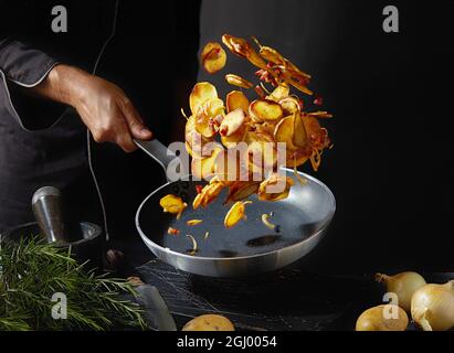 Faites cuire à la poêle des pommes de terre rôties à l'oignon par un chef masculin anonyme tout en cuisant le déjeuner sur fond noir Banque D'Images