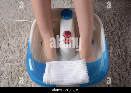 Pieds féminins dans un masseur vibrant. Bain de pieds à massage électrique. Détendez-vous après le travail. Pédicure et soins des pieds Banque D'Images