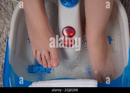 Pieds féminins dans un masseur vibrant. Bain de pieds à massage électrique. Détendez-vous après le travail. Pédicure et soins des pieds Banque D'Images
