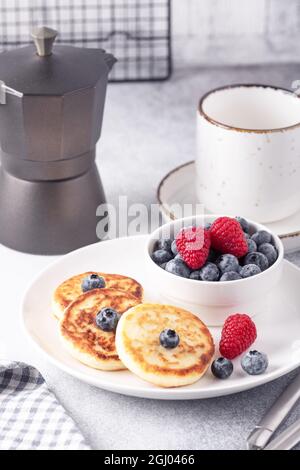 Crêpes au fromage cottage avec baies fraîches, une tasse de café et une cafetière sur une table en pierre. Délicieux petit déjeuner. Photo verticale - image Banque D'Images