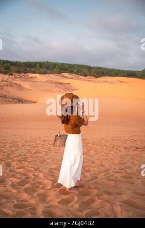 Arrière de la jeune femme asiatique portant un chapeau debout sur une dune du désert le soir Banque D'Images
