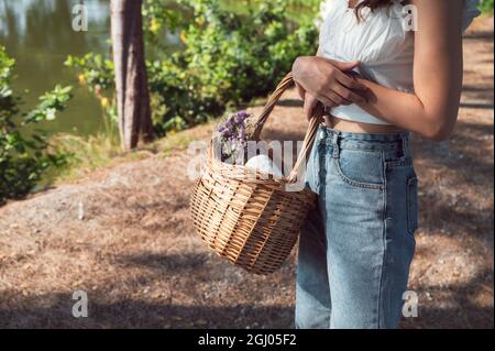 Femme asiatique tenant un panier en rotin avec fleur et tissu pour pique-niquer sous le soleil Banque D'Images