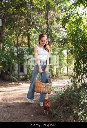 Jeune femme asiatique appréciant avec tenir le panier en rotin et la poule dans le jardin sur ensoleillé Banque D'Images