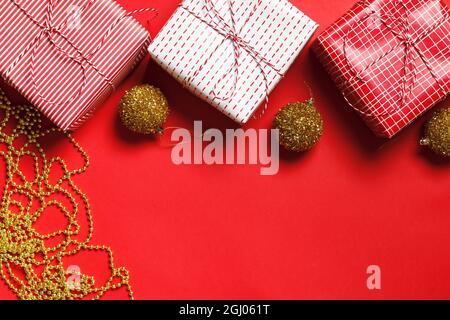 Composition de Noël. Boîtes-cadeaux, boules de Noël dorées et perles sur fond rouge. Flat lay, vue de dessus, espace de copie Banque D'Images