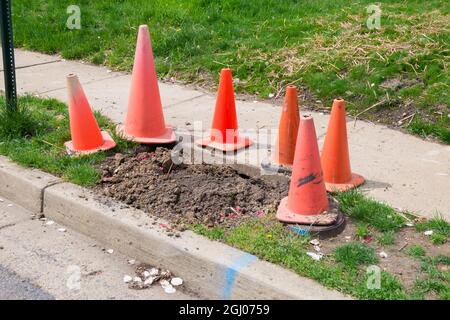 Des cônes orange entourent un petit site de terre excavée à côté d'un trottoir et d'une rue résidentielle. À Arlington, Virginie. Banque D'Images