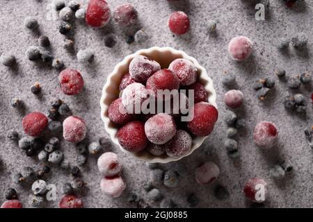 Mélanger les baies congelées à la cerise aigre rouge et au cassis dans un bol blanc sur fond gris. Vue de dessus. Banque D'Images