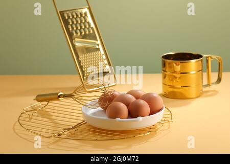 Outils de cuisine avec fouets en or, grille de refroidissement, râpe et plaque à œufs sur la table. Banque D'Images