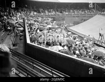 Les arrêts de pluie jouent à Wimbledon vue des terrains couverts pendant la pluie d'aujourd'hui avec des foules portant des parasols et des couvre-chefs attendant des pauses par temps froid. 3 juillet 1952 Banque D'Images