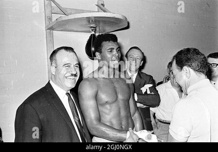 Champion du monde et responsable. Voici la photo d'aujourd'hui du champion du monde de poids lourd Cassius Clay (Mohamed Ali), dont les gants ont été retirés par son Manager Angelo Dundee à la suite d'une séance d'entraînement à la salle d'exercices de l'armée territoriale, White City, pour son combat de mai 21 avec le champion britannique Henry Cooper au stade de football d'Arsenal, à Highbury, Londres 12 mai 1966 Banque D'Images