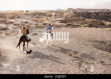 Jeune couple à cheval faisant l'excursion avec les animaux de compagnie de chien au coucher du soleil - foyer principal sur le dos de la femme Banque D'Images