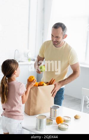 Homme souriant tenant la pomme près du sac en papier et de la fille dans la cuisine Banque D'Images
