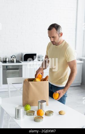 Homme prenant des fruits du sac de papier sur la table dans la cuisine Banque D'Images
