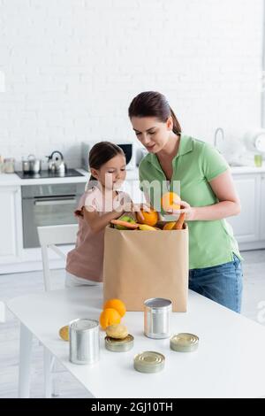 Femme et fille souriantes tenant la nourriture près d'un sac en papier dans la cuisine Banque D'Images