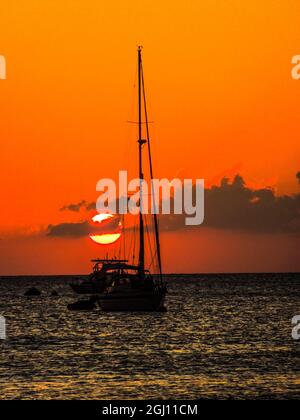 Seven Mile Beach, Grand Cayman. Voilier et un bateau avec le soleil orange se coucher derrière les nuages sur la mer des Caraïbes Banque D'Images