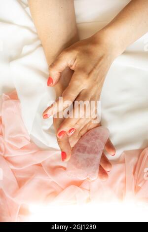 Cosmetologiste en uniforme médical rose tient des outils de beauté pour le massage de gua SHA chinois, fait de quartz rose naturel. Jeunesse et beauté. Procedure cosmétique Banque D'Images