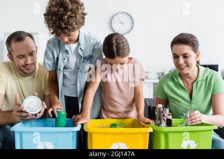 La famille avec les enfants trient les déchets dans des boîtes avec une affiche de recyclage à la maison Banque D'Images