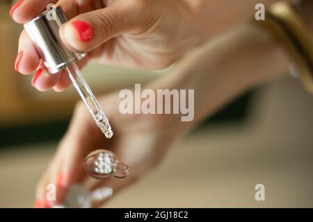 La main femelle tient le compte-gouttes. Sérum de beauté. Bouteille d'acide hyaluronique avec pipette avec goutte, antivieillissement cosmétique dans la main d'esthéticienne sur doror backgro Banque D'Images