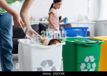 Femme tenant une bouteille près d'une poubelle avec une affiche de recyclage à la maison Banque D'Images