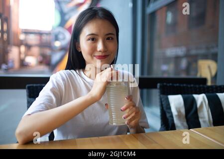 Une jeune femme asiatique boit du soda à la limonade au café en plein air et sourit Banque D'Images