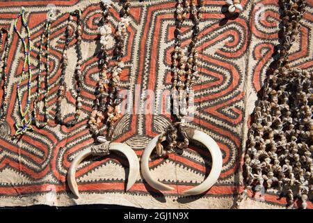 Papouasie-Nouvelle-Guinée, Tufi. Colliers de coquillages avec défenses de sanglier sur tissu traditionnel de tapa fait à la main, en papier mûrier, peint à la main avec natur Banque D'Images